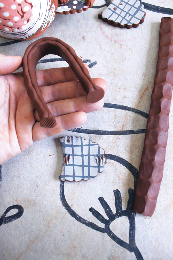 14 After adding marks with your thumbs to the top coil, shape the coil into an arch. Press the ends flat against the table.