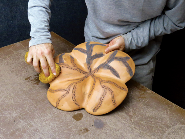 11 After bisque firing, apply black stain into the incised and carved designs, then wipe the excess away with a damp sponge.