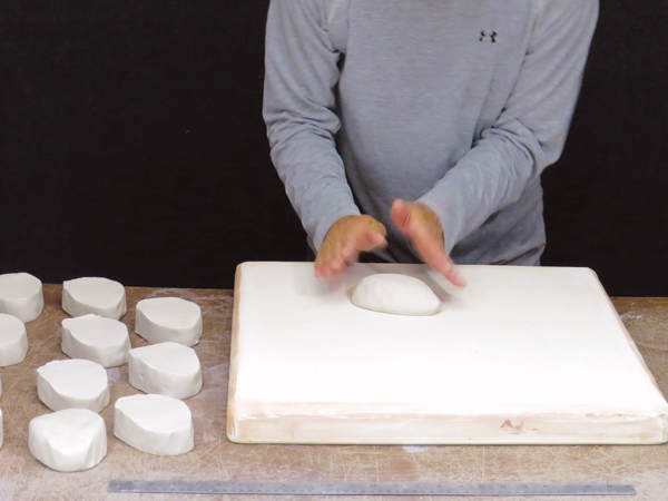 12 Working on a plaster bat, round the top of a slab cut from a teardrop-shaped coil.