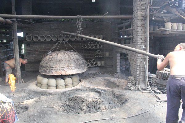 4 The wok cover is cantilevered into alignment with the sunken kiln base as the worker on the left bends to turn on the forced air.