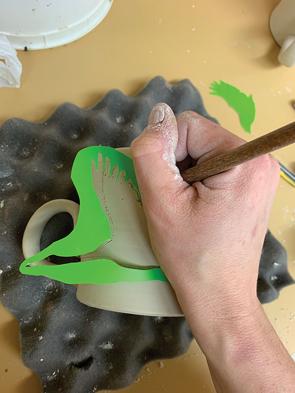 1 Draw the outline of a crane onto the sides of your cup with a plastic stencil and needle tool.