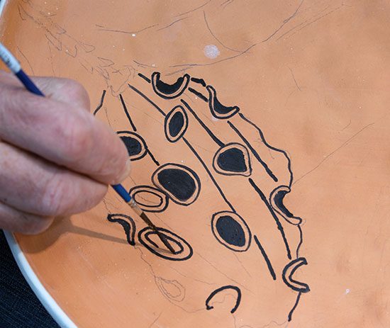 1 Apply cuerda-seca wax resist to the bisque-fired plate with a liner brush. The pencil drawing serves as a rough guide.