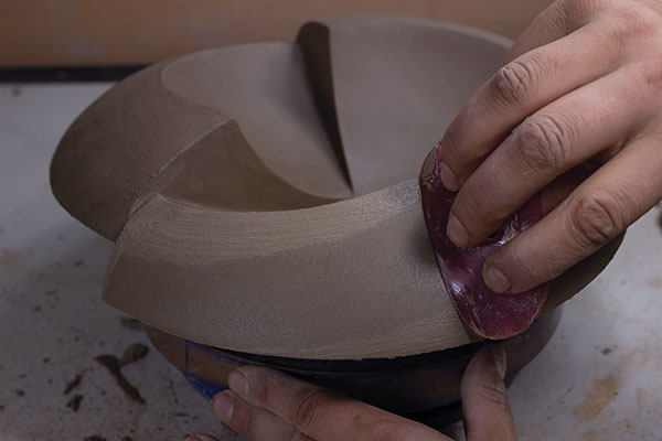 23 Use a serrated metal rib to refine the edges. Next, use a saturated, slightly rough finishing sponge to wear down the grooves, leaving a light layer of slip on the surface. Finally, use a red rib and the slip as a lubricant to compress and burnish the surface smooth. Allow the piece to slowly dry.
