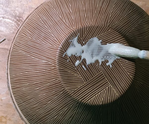 4 Paint an additional color of slip into the signature scratched into the rewaxed bottom.