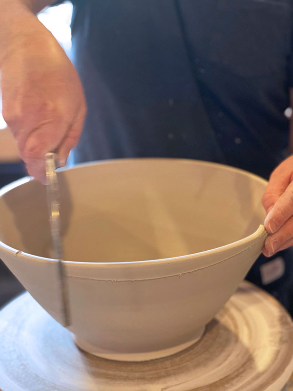 3 Line up two marks at a time on the rim and square the rim of the bowl with a confident slice that creates a clean path through the clay.