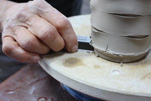 8 Place the basket on a banding wheel, and use the cut credit card rib to remove excess clay from around the base.