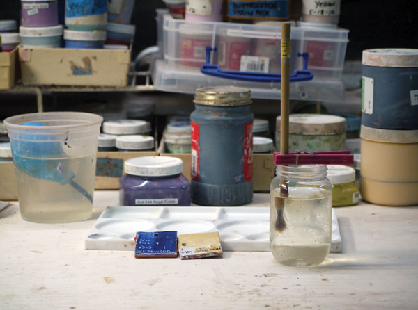 Linda Arbuckle’s studio brush holder is a converted watercolor brush washer that uses a recycled plastic jar instead of the perforated tray that is typically included with the holder. Her brush holder for travel consists of a simple container, in this case a glass jar, and spring clothespins to hold the brushes in place so just the bristles are submerged in water.